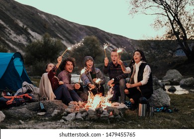 Multi races group of young teens at camping holding sparkling fireworks campfire on night party - Powered by Shutterstock