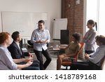 Multi racial businesspeople gather at briefing, positive team leader talking to office employees interns or students at corporate training teach explain project strategy discuss business plan concept