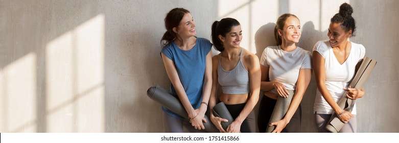 Multi racial girls wear active wear talking standing near wall holding personal mats wait for yoga session, wellness, weight loss, body care concept. Horizontal photo banner for website header design - Powered by Shutterstock