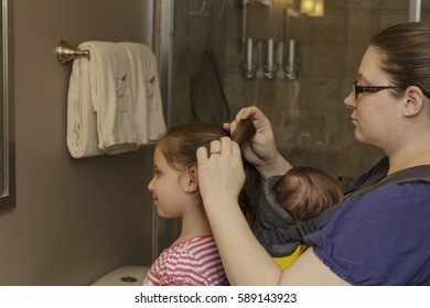 Multi Tasking Mother Fixing Daughters Hair With Baby On Her Chest