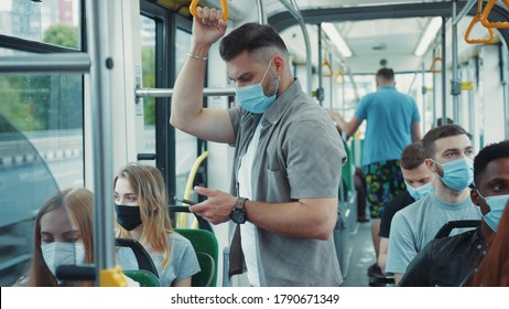Multi-age Caucasian People In Face Masks Protection Drive In Tram. Bearded Millennial Man Using Smartphone For Social Media In Public Transport.