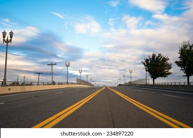 Multiband Wide Asphalted Road With A Dividing Strip Oncoming Traffic, Marked By The Yellow Line, Which Converge On The Horizon On A Background Of Street Lights And Silhouette Of Trees Along The Road.