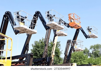 Multicolor aerial working platforms of cherry picker against blue sky.