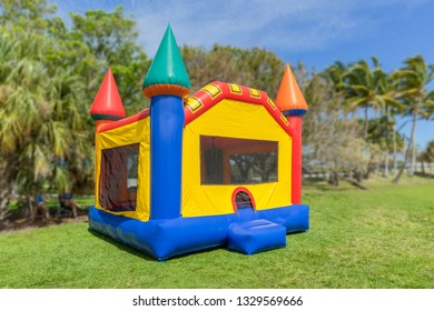 A multi-color castle bounce house photographed from the left side. The inflated bounce house has pops of color everywhere sits at the park on a beautiful sunny day.