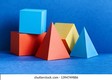 Vielfarbige geometrische Figuren bleiben Lebenszusammensetzung. Dreidimensionale Prismenpyramide, rechteckige Würfel auf blauem Hintergrund. Platonische Feststoffe, Einfachheitskonzept