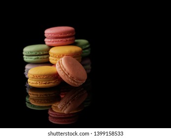 Multi-color macarons on the black background. Side view with reflection. Blank space.
