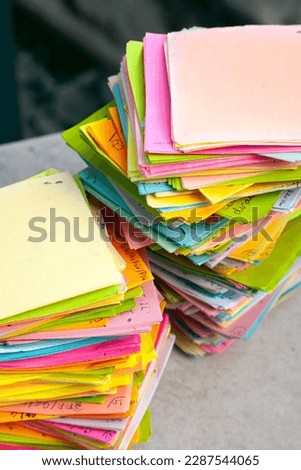 Multicolor memo notes with tasks stored chaotically in 2 stacks. Work overflow represented by a pile of note papers with tasks