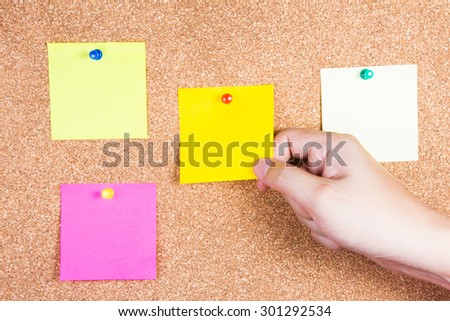 multicolor reminder sticky notes on cork board with hand holding, empty space for text