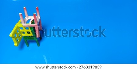 Multicolor small chairs placed in perspective order on blue reflective floor, minimal concept of waiting area, empty seating, playful educational furniture background with copy space.