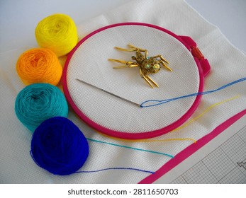 Multicolor threads, a needle, and a golden spider on embroidery fabric; a hobby.
