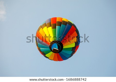 a multicolored balloon in a blue sky with clouds a close up view of the basket with pilots from below