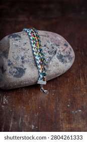 Multicolored beaded bracelet with braided threads on stone on old brown wooden table background. Vertical shot, copy space.