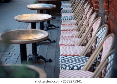 Multi-colored beautiful wicker chairs stand on a city street along the brick wall of a restaurant on a background of wooden round tables - Powered by Shutterstock