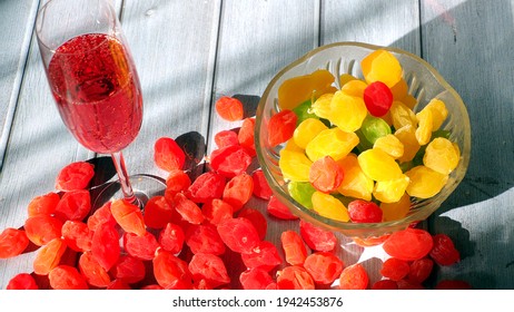 multicolored candied fruits and a glass with a pink drink on a wooden table