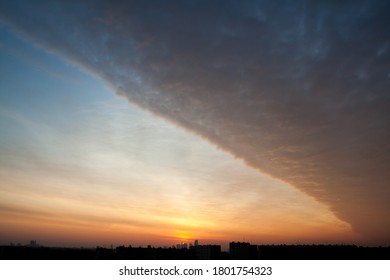 Multi-colored clouds in the light of the setting sun over the tops of urban buildings

