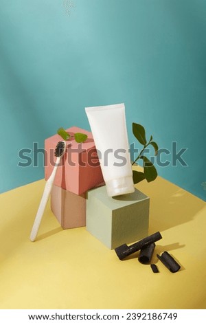 Multicolored cubes are placed next to each other. A white cosmetic tube is displayed with a toothbrush, bamboo charcoal and green tea. Blue-yellow background. Copy space for ads.