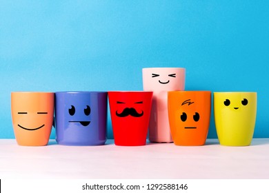 A lot of multi-colored cups with funny faces on a blue background. The concept of a friendly company, a big family, meeting friends for a cup of tea or coffee, father's day, office, boss day.