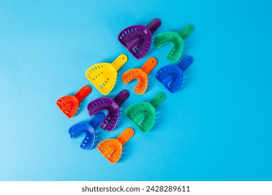 Multi-colored dental spoons for taking an impression of the dental jaw on a blue background. Orthodontics in dentistry. Dental prosthetics and crown manufacturing. Copy space for text