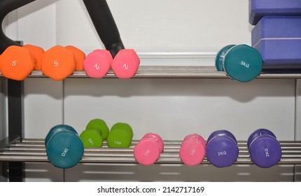 Multicolored dumbbells on metal shelf in sport fitness center. Weight training equipment and sport activity concept.
					
					2 kg, 5 kg, 3 kg and 1 kg dumbbells or barbells.