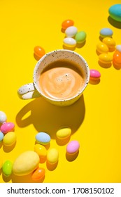A lot of multi-colored Easter eggs and a mug of coffee with froth on a yellow background. Happy Easter card with copy space for text. Minimal style. In a hard light. selective focus. Art style