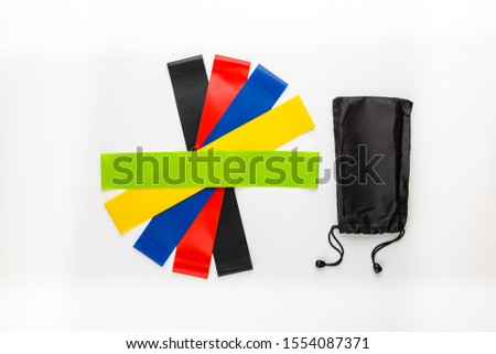 Multi-colored elastic rubber bands for fitness on a white background. A set of rubber bands of different colors - yellow, green, red, blue and black with a bag for storing them.