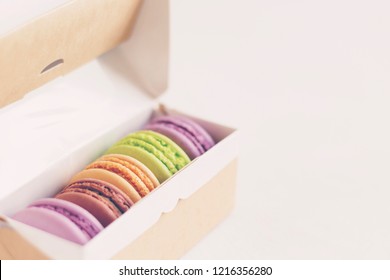 Multicolored French Macarons In Craft Packaging On White Background, Toned. Confectionary, Sweets, Bakery, Cooking, Delivery, Present, Menu Concept. Copy Space, Close-up, Layout Design 