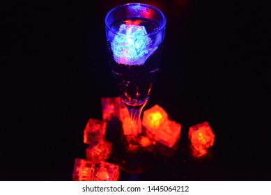 Multicolored glowing ice cubes float in a crystal champagne glass that illuminates the drink in it.
