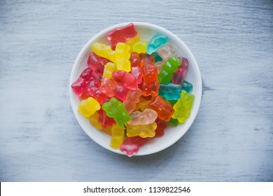 Multicolored gummy bears in a bowl. Heap of jelly candy bears on white wooden background. 