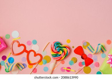 Multicolored heart shaped lollypop and decorative paper eye glasses on stick for photosession, gift boxes on pink background with blank space for text. Valentine's day or party concept. 