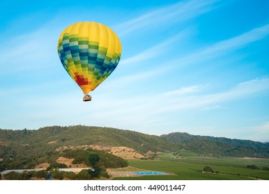 Multicolored hot air balloon floats in blue sunny sky over Norther California vineyards
