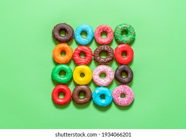 Multicolored icing doughnuts arranged symmetrically in a square on a green background. Homemade chocolate donuts decorated with sprinkles and colored icing.