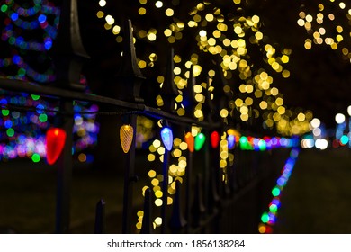 Multicolored lights line a wrought iron fence on a sidewalk