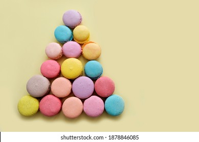Multicolored macarons on a yellow background. Composition in the form of a pyramid, Christmas tree, festive decor. Desserts concept