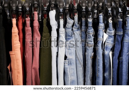 multi-colored men's and women's trousers on hangers in a clothing store. colorful pants store, new clothes during shopping, colorful men's and women's pants on hangers in a retail store