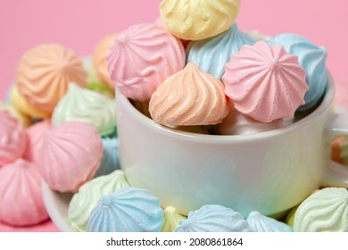 Multicolored meringues on a pink background. A teacup overflowing with colored meringues. - Shutterstock ID 2080861864