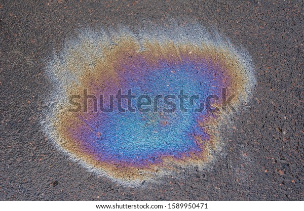 Multi-colored oil stain on\
the pavement. Rain blurred car oil from a malfunctioning car in a\
parking lot. Texture of asphalt and rainbow stains. Abstract\
background.