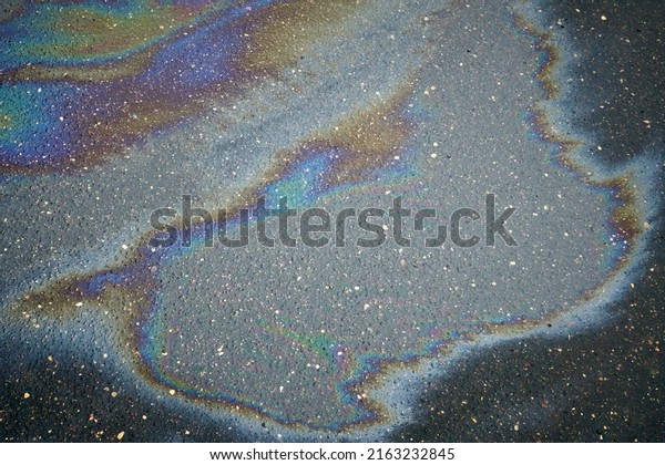 Multi-colored oil stain on the pavement. Rain\
blurred car oil from a malfunctioning car in a parking lot. Texture\
of asphalt and rainbow stains. Abstract background. Environmental\
pollution concept
