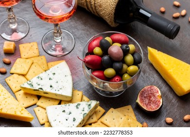 Multi-colored olives in a glass bowl. Cheese and biscuits and half a fig. Bottle of wine and two glasses of red wine. Top view. Brown background. - Powered by Shutterstock