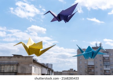 Multicolored paper origami bird cranes hanging on the window against the background of the sky. Origami crane in Japanese style is a symbol of happiness and prosperity. Fake birds flying
