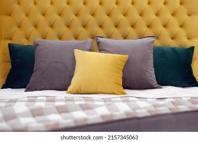 Multicolored pillows lie on a bed with a soft yellow velvet headboard with capitones and a checkered bedspread. Full screen photo with center focus