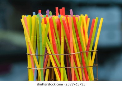 Multi-colored, plastic, disposable drinking straws with bellows standing upright in a wire container.  - Powered by Shutterstock