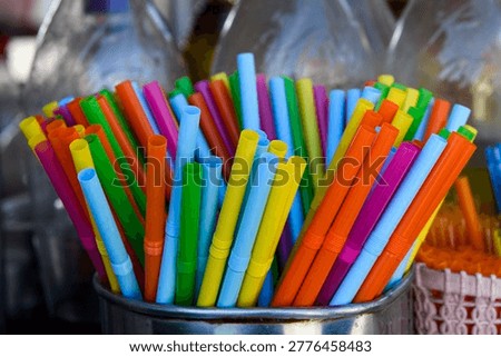 Multi-colored, plastic, disposable drinking straws with bellows standing upright in a shiny, silver metal container. 