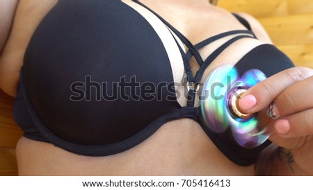 A multicolored, red-yellow-blue hand spinner or spinner, rotating on the person's arm. A woman spinning a spinner on a wood background near her lush breasts in a bikini.