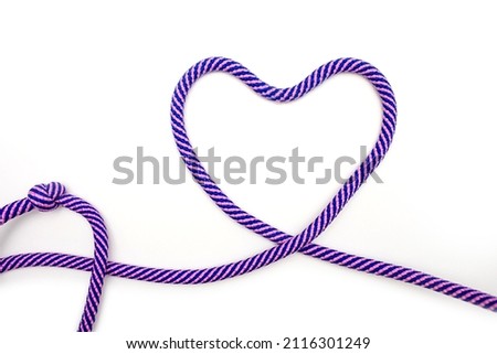 Multicolored rope with a heart shape on a white background. A blue-pink rope is twisted into a heart shape on a paper background. Love concept or wedding decor in minimalist style