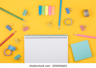 Multicolored set of pencils and blank notepad and office supplies  laying on yellow background top view. Creative set for hobby