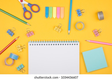 Multicolored set of pencils and blank notepad and office supplies  laying on yellow background top view. Creative set for hobby