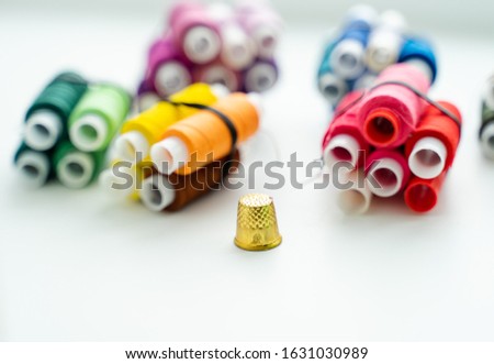 Multicolored spools of thread and thimble on a white background. Grouped by color
