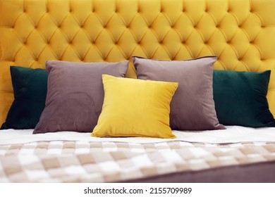 Multi-colored square pillows lie on the bed with a soft yellow velvet headboard with capitones. Selective focus.