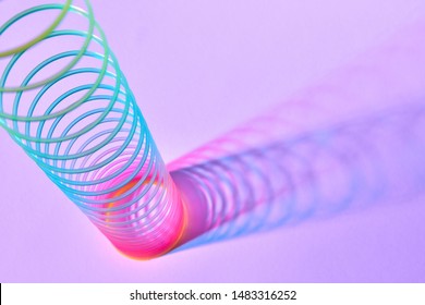 Multicolored statching plastic spiral toy with duotone shadows on a pink lavender background, place for text.