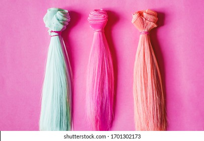 Coiffure multicolore droite, perruques pour poupées faites à la main sur fond rose. Travail à la main, passe-temps, concept de loisirs. Vue de dessus. Brins de cheveux colorés.